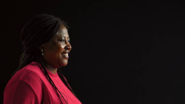 Pewna siebie afrykańska kobieta pozuje do cudownego zdjęcia portretowego w genialnym różowym swetrze. Widok z boku młodej czarnej kobiety ubranej w modną odzież uśmiechniętą do aparatu fotograficznego. - Zdjęcie, obraz