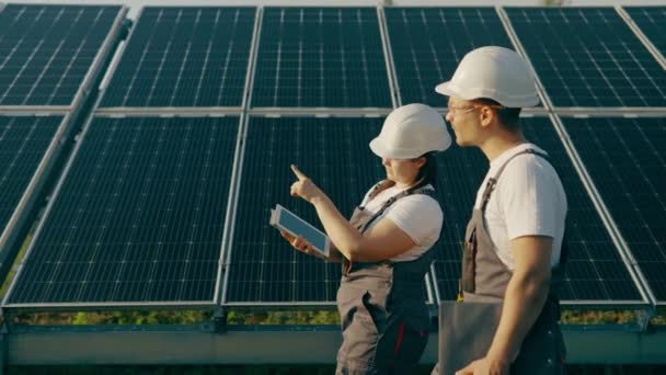 Workers in overalls at the production of alternative electricity collect and analyze data.Energy production using solar panels,green energy.Solar panels of an ecological power plant placed in a field - Footage, Video