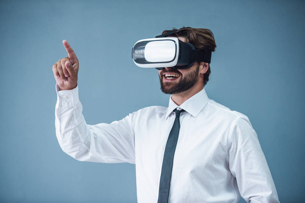 Bonito empresário barbudo em terno formal está usando óculos de realidade virtual 3d e sorrindo, em fundo cinza
 - Foto, Imagem
