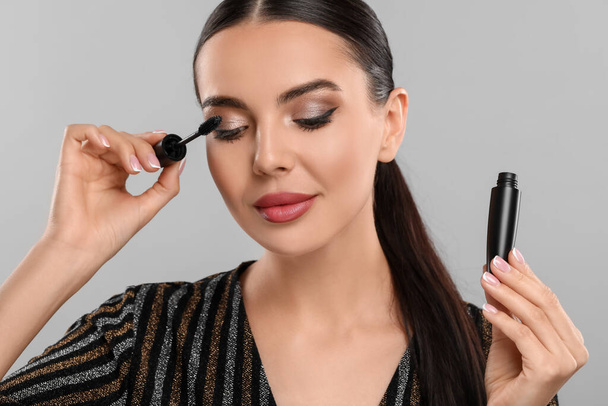 Everyday makeup. Beautiful woman applying mascara on light grey background - 写真・画像