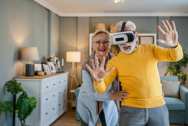 man mature senior caucasian male husband with his wife senior couple at home enjoy virtual reality VR headset - Photo, Image