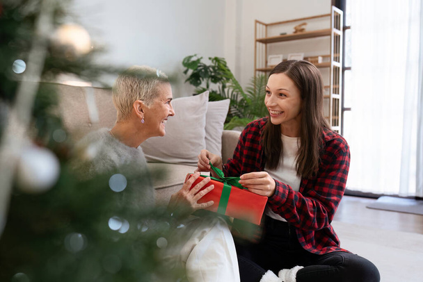 Hija regalo abierto de la madre de la Navidad mientras está sentado en el suelo en casa. - Foto, Imagen