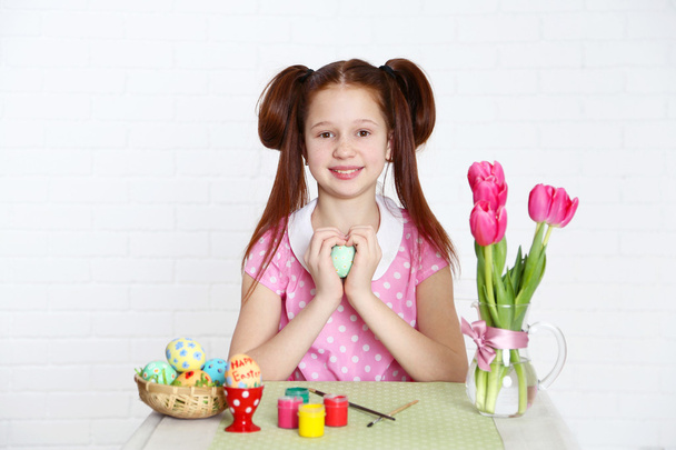 Cute girl decorates Easter eggs, on light background - Fotografie, Obrázek