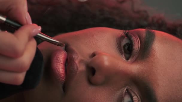 Make-up kunstenaar het aanbrengen van lippenstift op de lippen van een jong aantrekkelijk model in een fotostudio. Langzame beweging. - Video