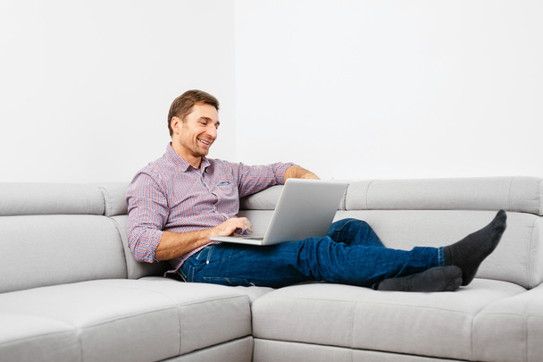 Man on sofa using laptop - Фото, изображение
