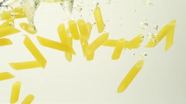 Movimiento lento de Penne rigate salpicadura de pasta cayendo en agua hervida sobre fondo blanco - Imágenes, Vídeo