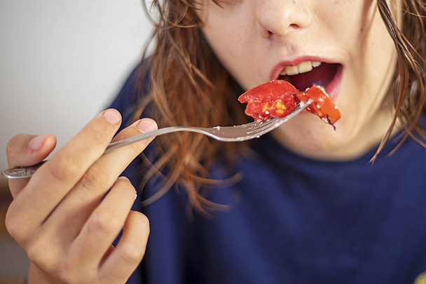 adolescente feliz comiendo rodajas de tomate rojo con un tenedor con la boca abierta - Foto, Imagen