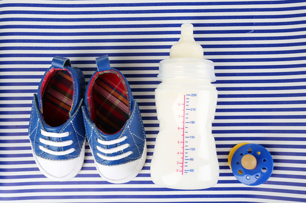 Baby shoes with nipple and bottle of milk on blue background - Foto, afbeelding
