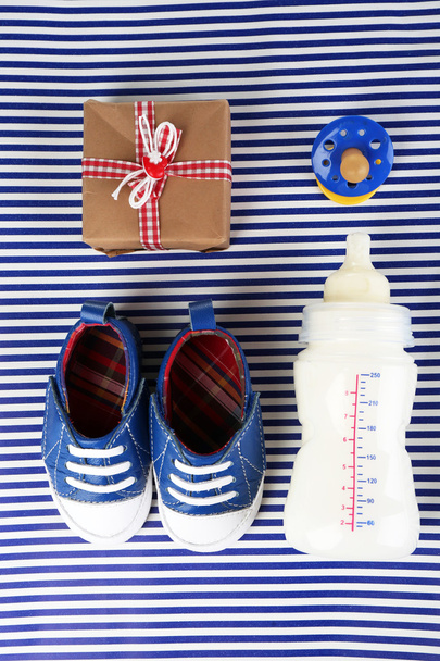 Baby shoes with gift and bottle of milk on blue background - Foto, Imagen