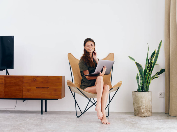 Estudante do sexo feminino estudo senta-se em uma cadeira com um trabalho laptop em casa sorrir e relaxar, moderno estilo de vida escandinavo interior elegante, espaço de cópia. Foto de alta qualidade - Foto, Imagem
