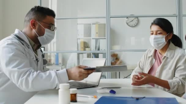 Cintura para arriba de la joven hispana firmando un acuerdo médico mientras tiene cita con su hija pequeña en una clínica moderna - Metraje, vídeo