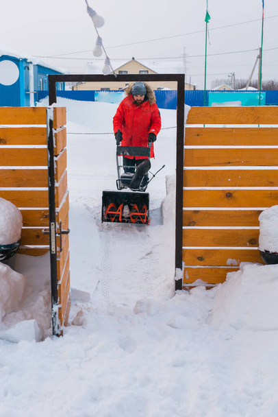 Egy ember, aki hófúvóval takarítja a havat az udvarról. Téli szezon és hófúvó berendezések. - Fotó, kép