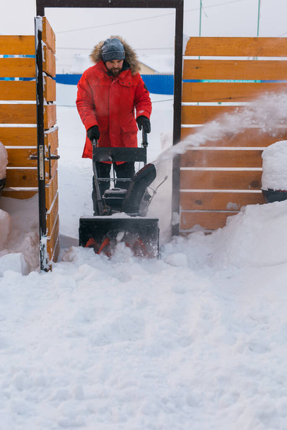 Ένας άντρας με καθαρό χιόνι από την πίσω αυλή με φυσητήρα χιονιού. Χειμερινή περίοδος και εξοπλισμός φυσητήρων χιονιού. - Φωτογραφία, εικόνα