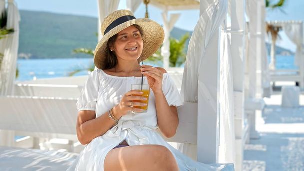 Portrait d'une femme brune élégante se relaxant au restaurant de la plage de la mer et boire du jus d'orange ou un cocktail avec de la paille pendant les vacances d'été. - Photo, image