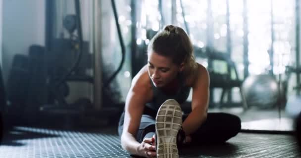 Kobieta, fitness i rozciąganie na podłodze w siłowni przygotowuje się do treningu, ćwiczeń lub treningu w pomieszczeniach. Aktywna kobieta w rozgrzewce ciała, rozciągnięciu nogi lub mięśniu w przygotowaniu, zdrowiu i wellness. - Materiał filmowy, wideo