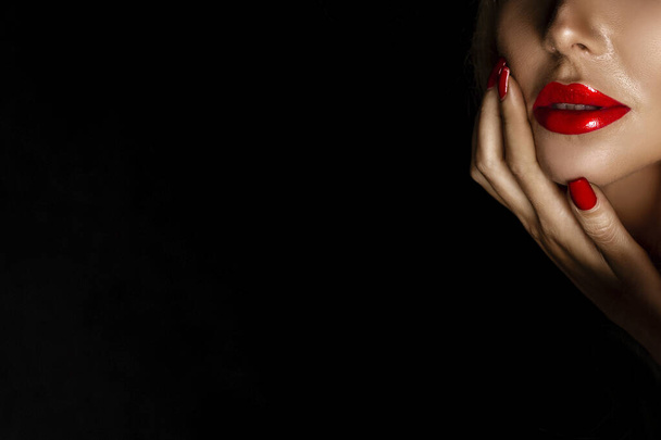 Belle femme dans un maquillage élégant avec des lèvres et des ongles rouges posant sensuellement sur un fond noir. - Photo, image