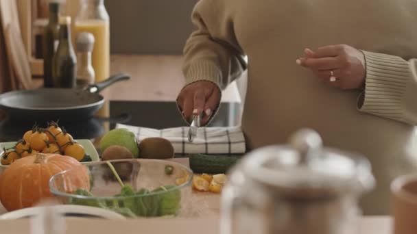 Keskiosa tunnistamaton raskaana oleva nainen neulottu beige mekko leikkaamalla tuoreita kurkkuja ja tehdä terveellisiä vihanneksia salaatti kulhoon lounasaikaan - Materiaali, video