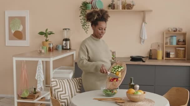 Keskikokoinen laukaus nuori raskaana oleva afroamerikkalainen nainen sekoittamalla ainesosia kulhoon ja tekemällä terveellistä kasvissalaattia lounaaksi kotona - Materiaali, video