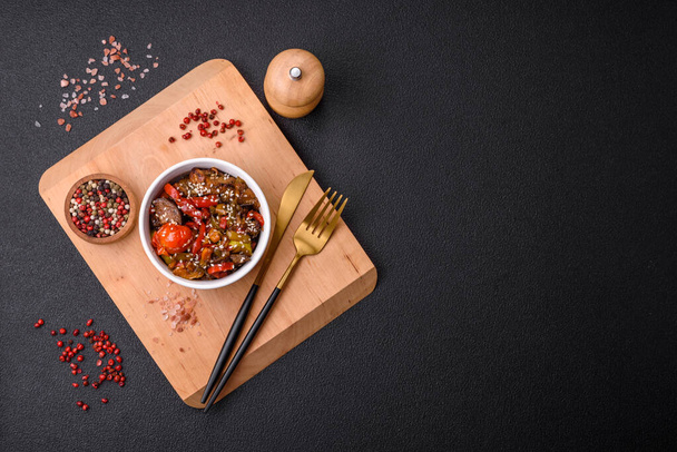 Теплый салат с телятиной, помидорами, перцем, цуккини, кунжутом, солью, специями и травами на темном бетонном фоне - Фото, изображение