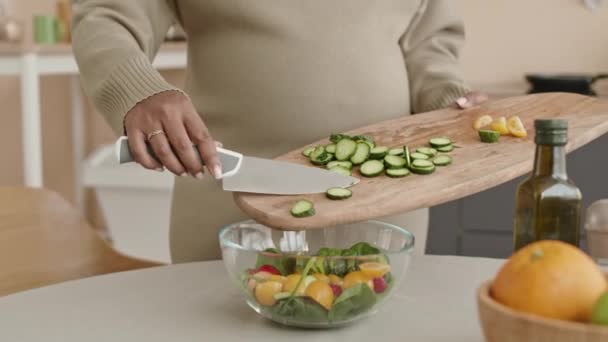 Plan moyen de jeune belle femme enceinte afro-américaine faisant de la salade de légumes frais dans un bol et caressant son ventre - Séquence, vidéo