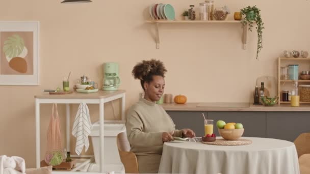 Medium shot van gelukkig jong zwanger Zwarte vrouw kijken naar baby echografie scan als zittend aan keukentafel in mooi appartement - Video