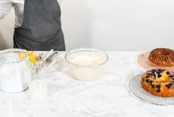 Combinare abilmente gli ingredienti con un mixer a mano per preparare una ricca glassa al burro di crema di formaggio liscio, che è perfetto per adornare la torta bundt. - Foto, immagini