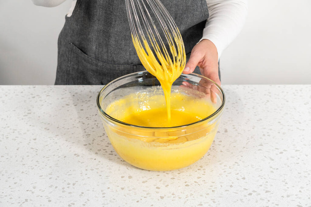 Het mengen van natte ingrediënten in een kleine glazen mengkom om een eenvoudige vanillegebakje te bakken. - Foto, afbeelding