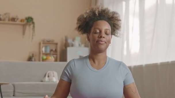 Tilt down van ontspannen jonge zwarte vrouw beoefenen yoga meditatie op de vloer in ruime studio appartement - Video