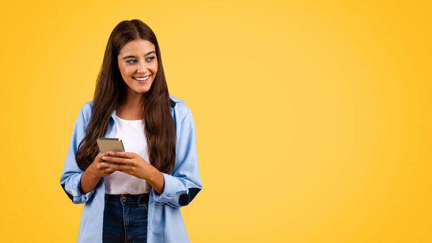 Щаслива біла студентка, яка вводить повідомлення по телефону, спілкується в соціальних мережах, дивиться на вільний простір, ізольована на жовтому тлі, панорама. Освіта та онлайн-додаток навчання - Фото, зображення