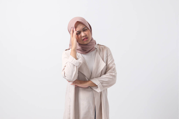Portret van een overweldigde Aziatische hijab vrouw in casual pak aanraken van haar hoofd, het hebben van hoofdpijn, en het gevoel van stress. Zakenvrouw concept. Geïsoleerde afbeelding op witte achtergrond - Foto, afbeelding