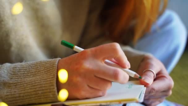 Close-up hand van Rood harig meisje, vrouw, tiener in gezellige trui schrijven in haar dagboek kerstvakantie. Creëer gedachten en dromen, plannen voor volgend jaar. Reflectie van een jonge volwassene. Positieve emoties - Video