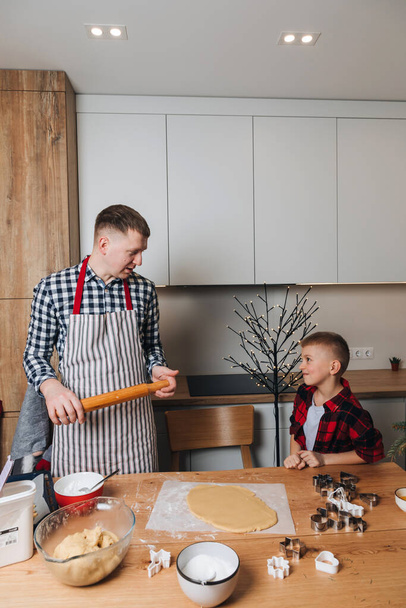 Vater und Sohn an einem Holztisch in der Küche backen Kekse, geformtes Mehl. Frontansicht - Foto, Bild