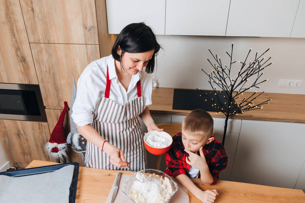 Mom and son are kneading dough for cookies at a wooden table in the kitchen. Cooking desserts at home. Joint activities with children. Top view - Photo, Image