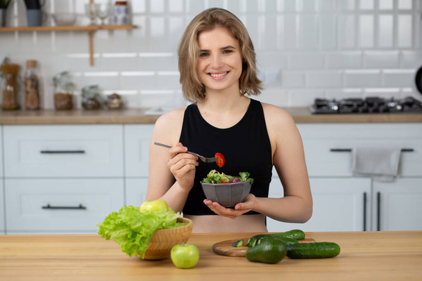 Красивая молодая женщина ест салат на кухне дома. Закрыть красивые девушки едят здоровый салат, здоровый образ жизни - Фото, изображение