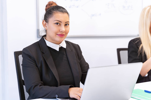 Профессиональная деловая женщина, работающая с ноутбуком, сидящая на столе в офисе. Концепция бизнеса. - Фото, изображение