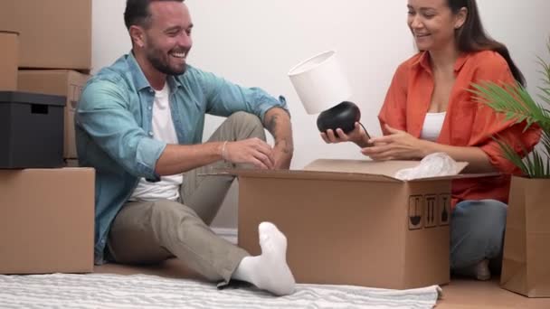Usmívající se pár si užívá útulný okamžik, zatímco vybaluje krabice ve svém novém bytě. Budování společného života, dojemné denní štěstí - Záběry, video