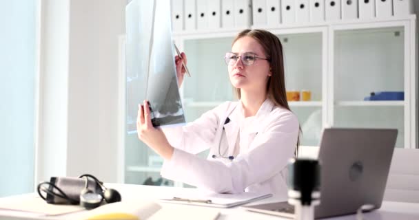Studente medico esamina i raggi X del paziente in ospedale. Terapista femminile con stetoscopio che guarda i raggi X - Filmati, video
