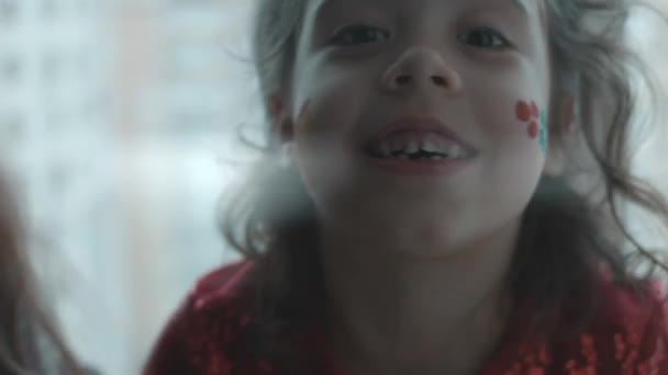 Весела маленька дівчинка з різдвяними тематичними картинами на обличчі. Подарункові та папороті картини на обличчі. Новорічна концепція - Кадри, відео