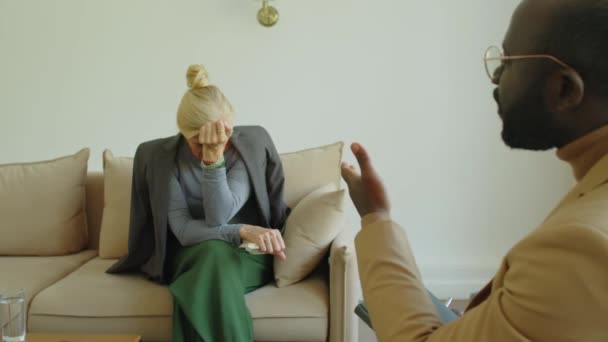 Por encima del hombro, una mujer mayor sentada en el sofá llorando mientras la terapeuta afroamericana hablaba con ella durante la consulta. - Imágenes, Vídeo