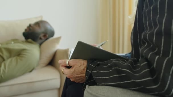 Обрізаний дуговий знімок жінки-терапевта записується в блокноті, слухаючи пацієнта під час консультації - Кадри, відео