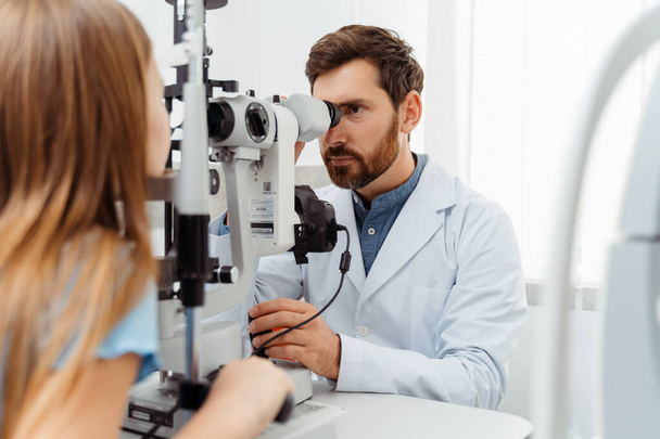 Lekarz badający oczy dziewczynki ze sprzętem okulistycznym w nowoczesnej klinice. Koncepcja opieki zdrowotnej - Zdjęcie, obraz