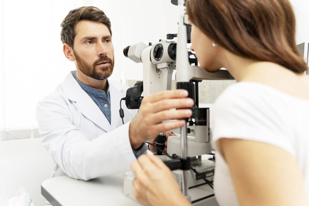 Férfi szemész binokuláris réslámpával, miközben a női beteg szemét vizsgálja. Orvosi vizsgálat - Fotó, kép