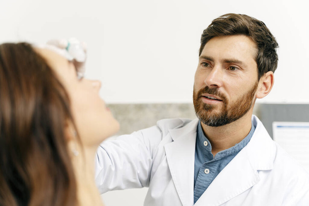 Pozorný samec optometristy kapající kapky do očí pacienta. Koncept zdravotní péče - Fotografie, Obrázek