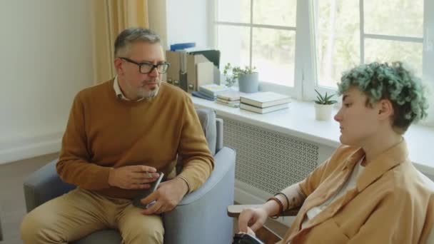 Starší mužský psycholog nabízející rady, jak se vyrovnat s depresí během konzultace s mladou pacientkou - Záběry, video