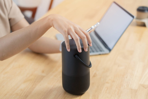 Selectieve focus van de hand van de vrouw met laptop met behulp van voice assistant speaker op kantoor. Draagbaar draadloos luidsprekerconcept. - Foto, afbeelding