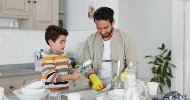 Ομαδική εργασία, πατέρας ή παιδί πλύσιμο πιάτων με υποστήριξη για την καθαριότητα σε ένα νεροχύτη κουζίνα στο σπίτι της οικογένειας. Χαμόγελο, σαπούνι ή αγόρι παιδί μάθησης, καθαρισμού ή βοηθώντας ένα ευτυχισμένο μπαμπά για υγιή υγιεινή μαζί. - Πλάνα, βίντεο