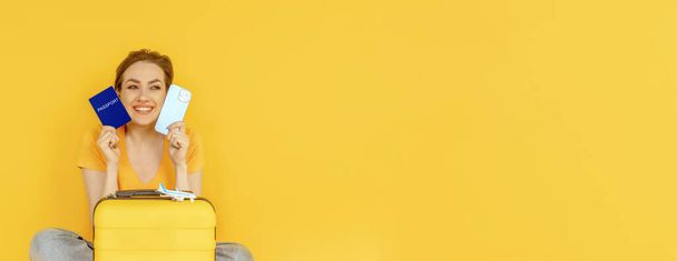 mujer feliz en camiseta amarilla con maleta, pasaporte y teléfono con billete electrónico sobre fondo amarillo. Espacio para el texto. Concepto de viaje - Foto, imagen
