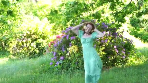 Retrato al aire libre de mujer pelirroja feliz en vestido verde y auriculares bailando en el parque público. Escuchar música en línea en cualquier lugar y ser tú mismo concepto - Metraje, vídeo