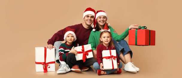 Glückliche Familie in Weihnachtsmützen und mit Weihnachtsgeschenken auf beigem Hintergrund - Foto, Bild