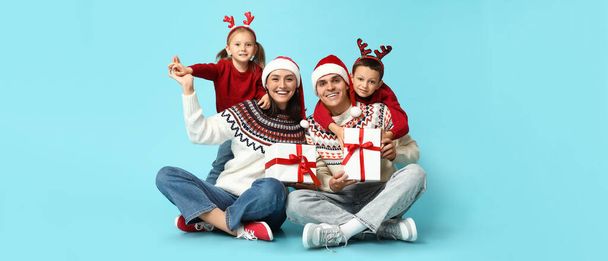 Gelukkig gezin in kerstkleding en met geschenken op lichtblauwe achtergrond  - Foto, afbeelding